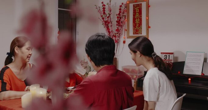 Slow motion shot Asian family members enjoying Asia food together while having reunion dinner in the dining room at home on Chinese lunar new year's eve.