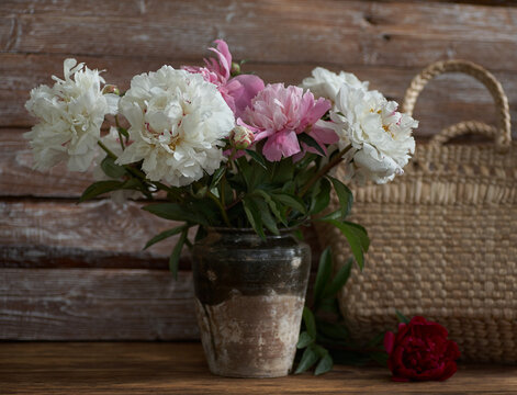 Still life with white and pink peonies in a old ceramic vase on wooden background