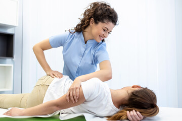 Young doctor chiropractor or osteopath fixing lying womans back with hands movements during visit...