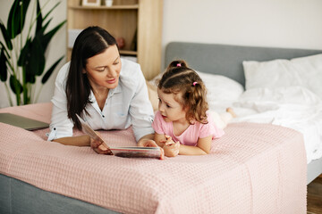 Happy mother and daughter reading a book together in bed. Time together, taking care of children