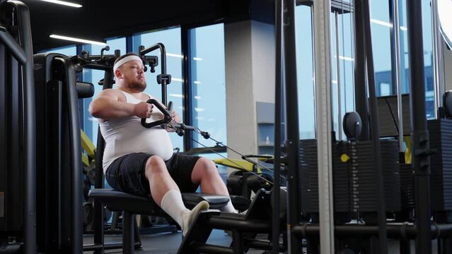 Overweight funny man lifting blocks, doing chest exercises, training on block device and gym equipment, fat burning.
