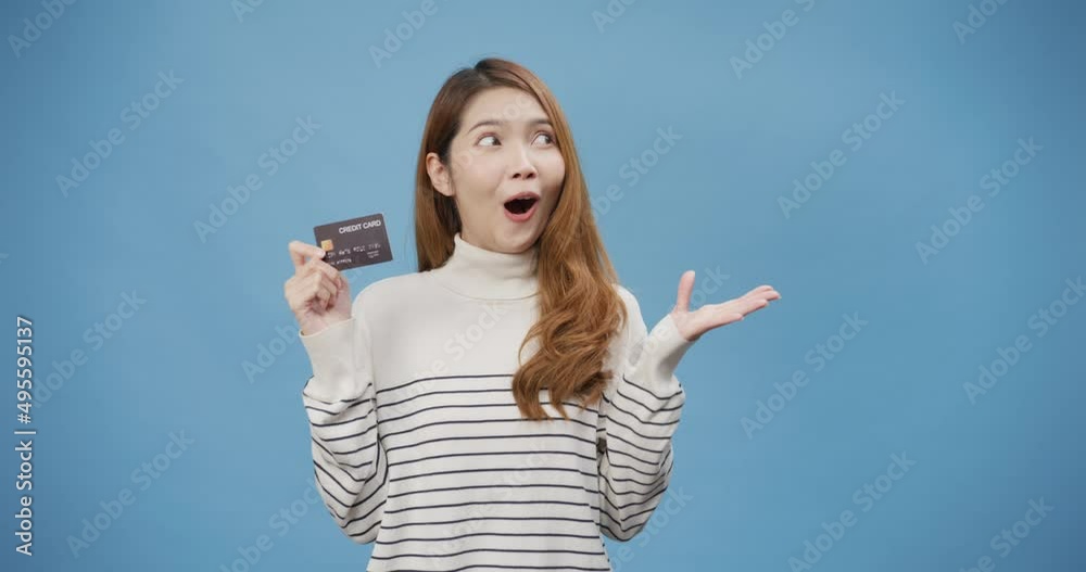 Wall mural Youth attractive cheerful Asia lady wear sweater hold atm or debit or credit card and using for online shopping stand isolated over blue background. Female thumbs up enjoy purchase copy space concept.