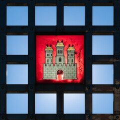 Bratislava city crest symbol, coat of arms in stained glass set in iron grid, backlit against clear blue sky 