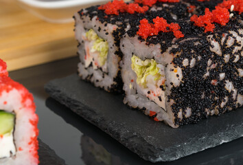 close-up of rolls with red and black flying fish caviar on a black wooden tray