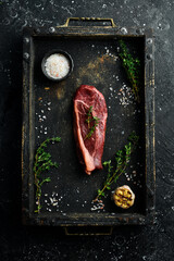 Classic Raw striploin steak. Fresh meat with seasonings. Aged steak. Top view. On a black stone background.