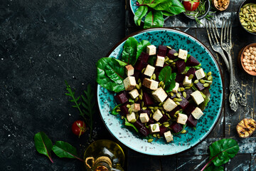 Vegetarian food in a bowl: Beet salad, tofu cheese, spinach and pumpkin seeds. The concept of healthy eating. On a black stone background. Top view.
