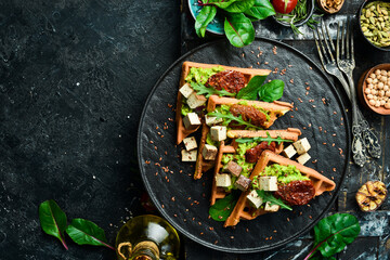 Waffle sandwiches with avocado pate, sun-dried tomatoes and tofu cheese. The concept of dietary nutrition. On a stone background.