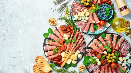 Antipasto plate of cold meat, prosciutto, parmesan cheese and blue cheese with grissini bread sticks. On a stone background.