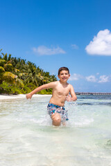 Funny boy running through the water on a tropical beach
