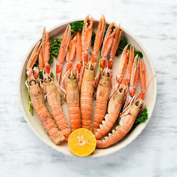 Boiled langoustines with parsley and spices on a plate. Norway lobster on a white wooden background. Top view. Free copy space.