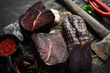 Dried veal beef with spices and herbs. On a black stone background. Top view. Free space for text.