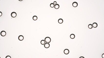 Small clear bubbles of hyaluronic acid attract each other creating bubble clusters against light grey background | Shot of moisturizer ingredients for its advertisement