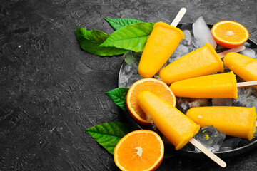 Orange popsicles on ice. Cold summer fruit sweets. On a stone background.
