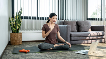 Young woman in sportswear is sitting on mat to prepare yoga exercise in the living room at home