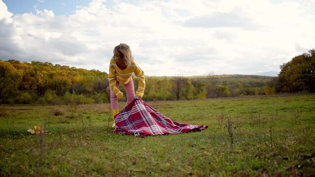 One girl holds a checkered plaid and walks slowly into the autumn forest. People are one with nature. Wellness concept. Health care, authenticity, a sense of balance and calmness.