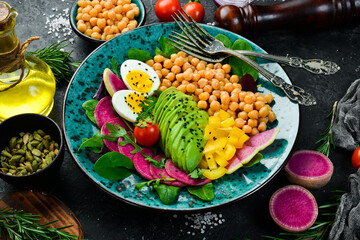 Balanced food: chickpeas, avocados, eggs, watermelon radishes and spinach. Buddha bowl tasty food concept on stone background.