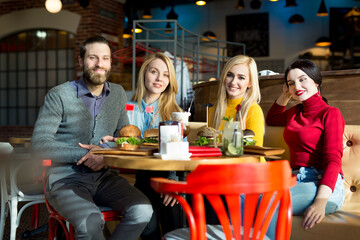 People have dinner together at a table in a cafe. Happy friends eat burgers and drink cocktails in the restaurant