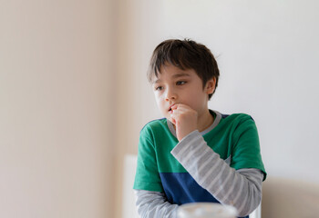 Emotional portrait young boy looking out deep in thought while eating nut, Cinematic portrait Child sitting alone with thinking face, Kid relaxing at home.