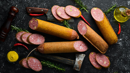 Sliced salami slices with rosemary and spices on a black stone background. Top view. Rustic style.
