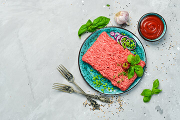 Raw mince beef, ground meat with herbs and spices on a plate. Top view. On a stone background.