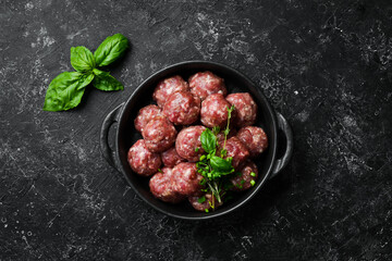Fresh raw beef meatballs with spices in a pan. Top view. On a stone background.
