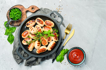 Mini grilled sausages on a frying pan. Barbecue. Meat menu. Top view. On a stone background.