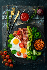 English breakfast: chickpeas, avocados, scrambled eggs, bacon vegetables on a black stone plate. Top view. Free space for text.