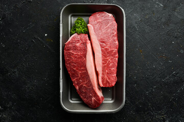 Raw rib eye steak of beef on a black stone background. Top view. Raw meat.