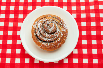 Cinnamon buns or cinnabon rolls, a homemade recipe for sweet traditional Danish dessert with white vanilla powder on red and white checkered background.