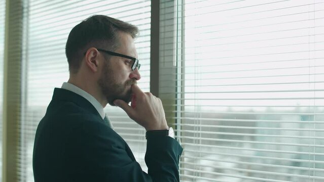 Focused creative man in a suit stands at the window in the office and reflects, the thinking process.
