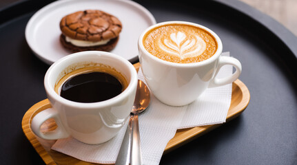 A cup of cappuccino and cup of coffee with chocolate biscuit on the black table in cafe. Close-up.