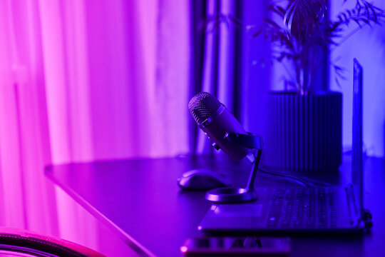laptop, smartphone, microphone on a black table. Home studio podcast interior. Microphone, laptop on the table. Online live radio studio desk with microphone in the foreground, entertainment concept