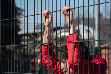 Boy child refugee behind a metal fence. Social problem of war migrants.