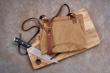 Brown fold apron on wooden board with knife. Selective focus