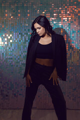 sexy young energetic woman in black suit in the studio against background of shiny squares