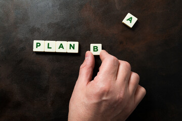 Hand placing the letter B next to the word PLAN on a dark background.