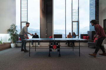 Two young start up business man playing table tennis at modern creative office space people group have meeting and brainstorming in background