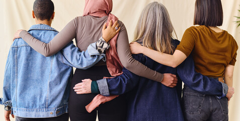 International Women's Day rear view portrait of four women standing with arms around each other in...