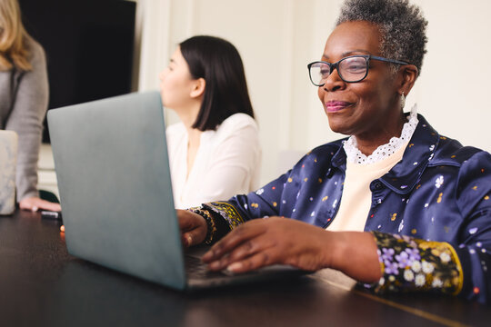 Portrait Of Senior Black Businesswoman With Short Gray Hair Wearing Glasses And Using Laptop