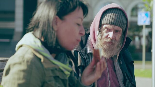 Senior homeless male hungrily looking at woman eating sandwich, hunger, crisis