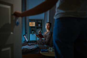 education, technology and people concept - teenage student girl with notebook and laptop computer learning in bed at home at night and mother entering room