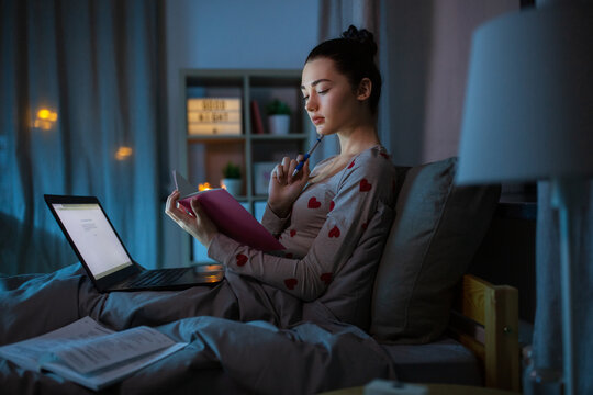 Education, Technology And People Concept - Teenage Student Girl With Notebook And Laptop Computer Learning In Bed At Home At Night