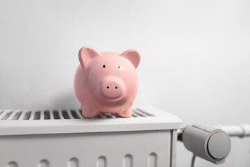 heating, energy crisis and consumption concept - piggy bank on radiator at home