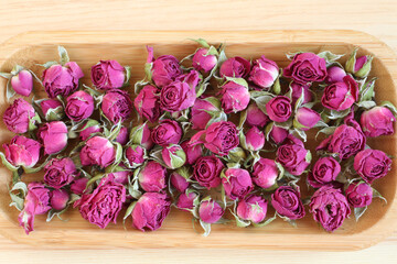 Dry rose flowers on a wooden plate on a wooden table. View from above.