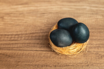 Three dark blue Easter eggs in a yellow straw nest on a brown background with natural textured wood