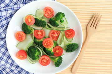Fresh vegetables salad with fresh cucumber slices, broccoli and tomatoes in white plate. healthy vegan and clean eating concept.