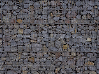 Decorative fence of bulk stone in the grid. Textured background of a stone wall with iron netting. Stone wall in wire frame. Gabion filled with limestone