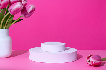 Pink round podium for product display on pink with tulips flowers in hard light