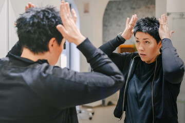 Woman fixing, styling short hair by the mirror. Daily beauty routine.