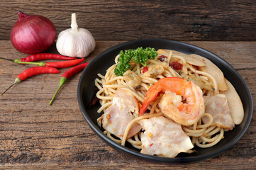 Homemade Stir fried spicy spaghetti with shrimp, clam, sausage, ham and dried chili on old wooden table. Asian meal concept.